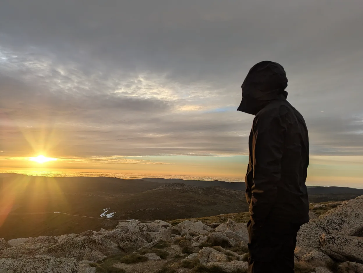 Hiker watching sunrise from Mt Kosciuszko summit, Kosciuszko National Park NSW